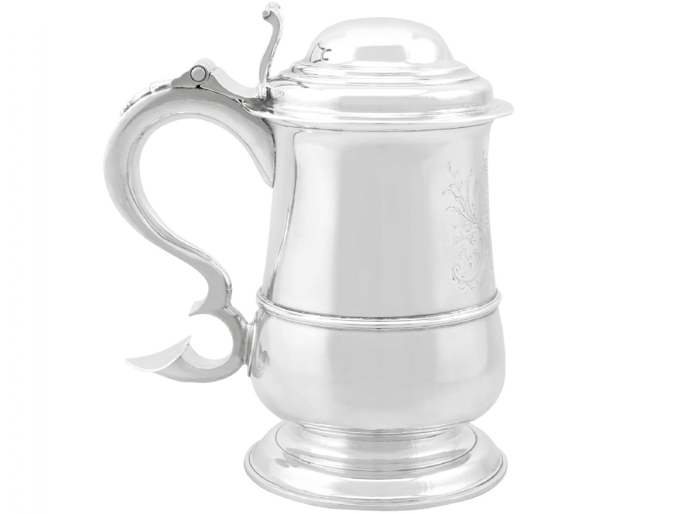 A George II sterling silver lidded tankard featuring a domed top, scroll handle, moulded girdle, and engraved foliage decoration.