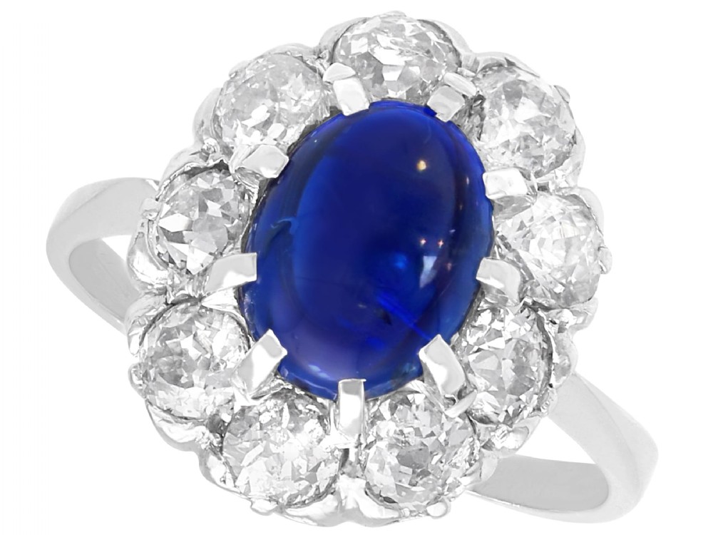 An antique 14ct white gold ring featuring an oval cabochon blue sapphire surrounded by a halo of round diamonds.