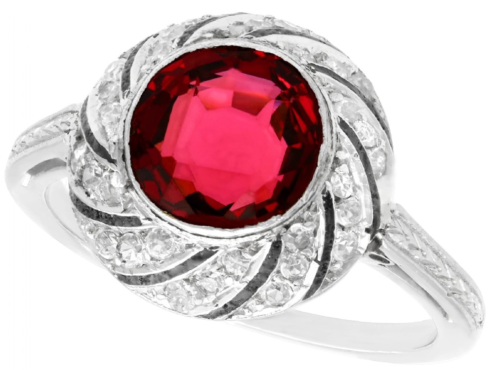 An Art Deco platinum dress ring featuring a central round red garnet surrounded by a swirling spiral bezel set with small diamonds.