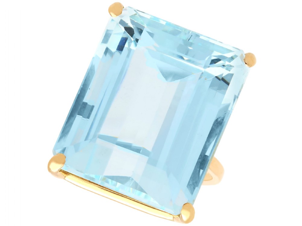 A substantial rectangular emerald-cut light blue aquamarine gemstone secured in a four-claw 18ct yellow gold ring mounting.
