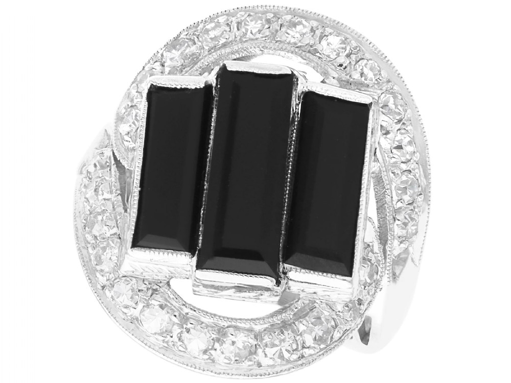 An Art Deco style platinum dress ring displaying three vertical rectangular black onyx plaques enclosed within a circular diamond-set halo frame.