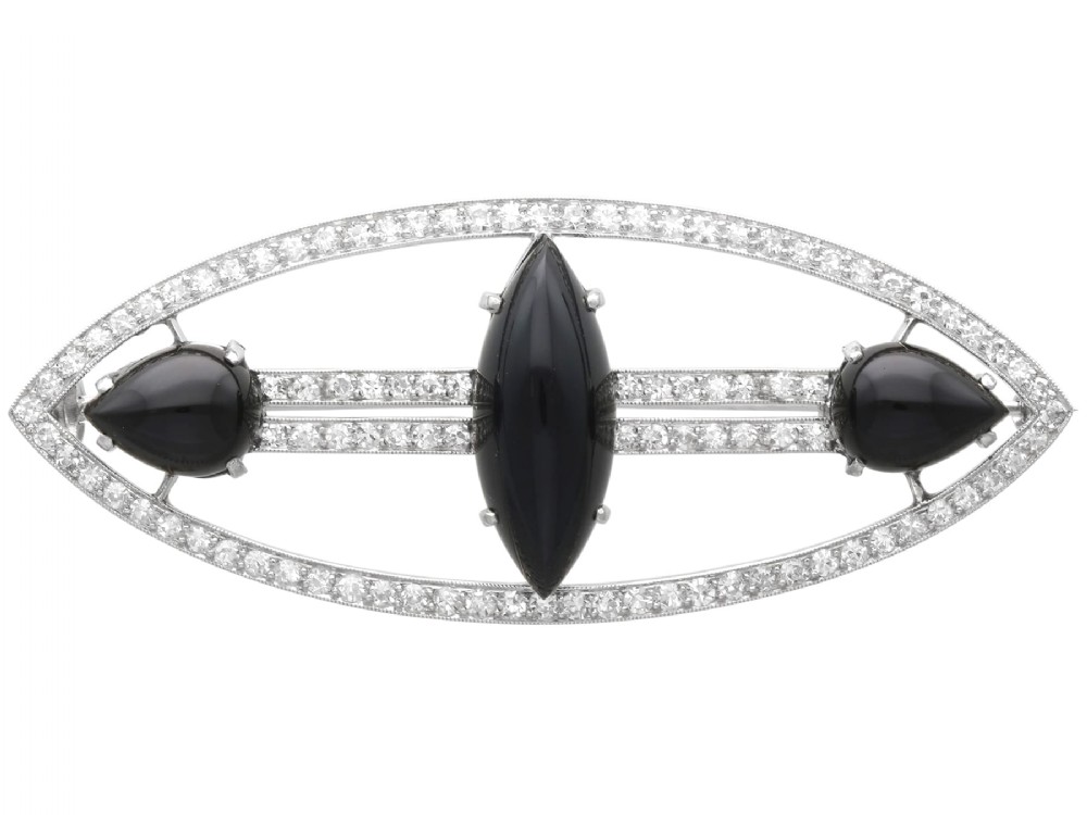An Art Deco platinum brooch featuring an openwork navette frame set with diamonds and three carved black onyx stones.