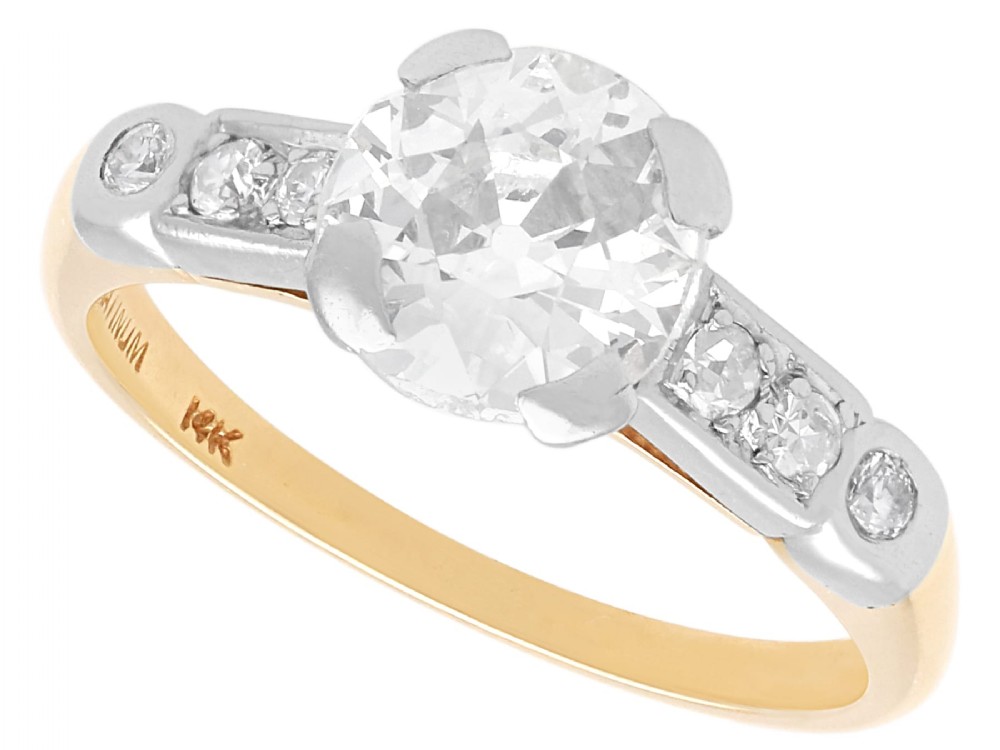 A round central diamond solitaire ring in a platinum claw setting with diamond-set shoulders on a 14ct yellow gold band.