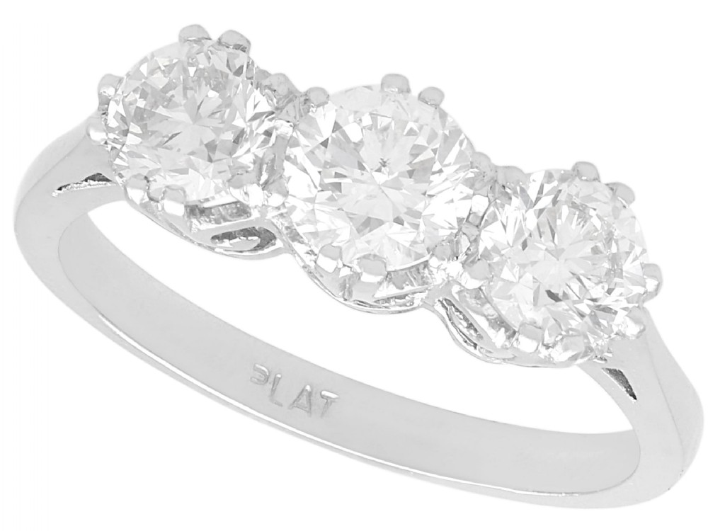 A platinum trilogy ring featuring three round brilliant diamonds set in individual claw mounts along a slender polished band stamped PLAT.