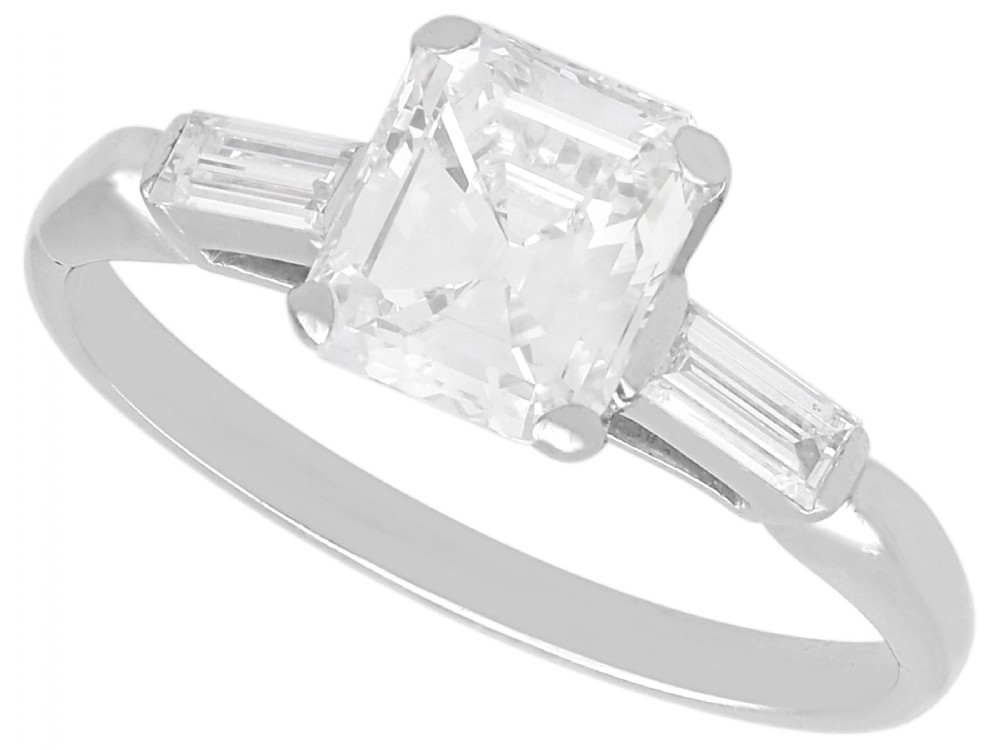A platinum solitaire ring featuring a central square step-cut diamond flanked by two baguette diamonds on a plain band.