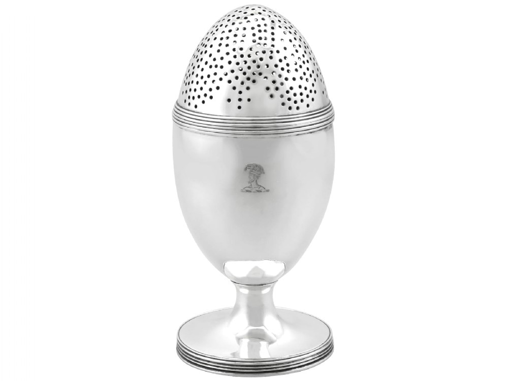 An egg-shaped George III sterling silver condiment caster featuring a perforated upper section, reeded borders, a small engraved crest, and a pedestal foot.