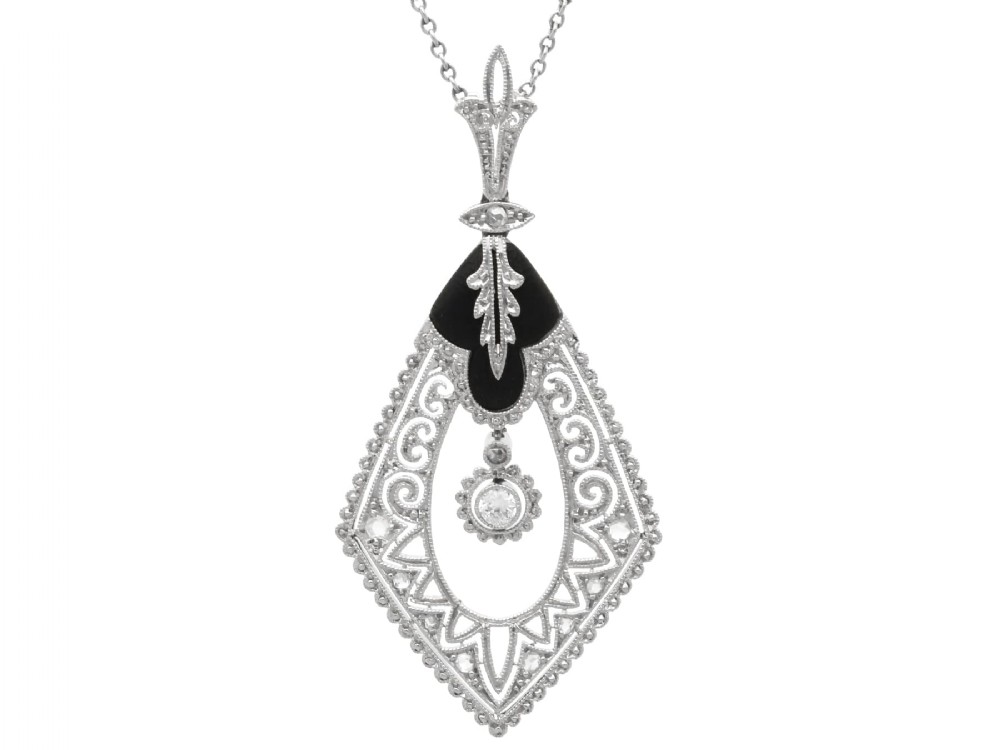 A diamond-shaped Art Deco platinum filigree pendant set with carved black onyx and a central suspended diamond drop.