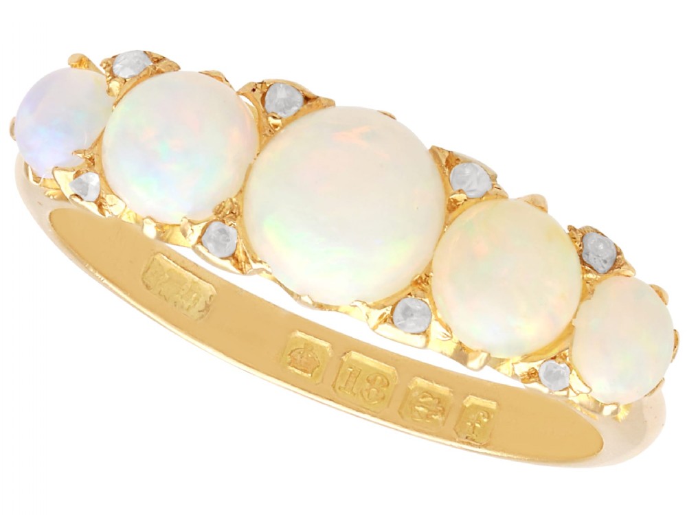 An Edwardian 18ct yellow gold five stone ring featuring graduated cabochon white opals with small diamond accents and full interior British hallmarks.