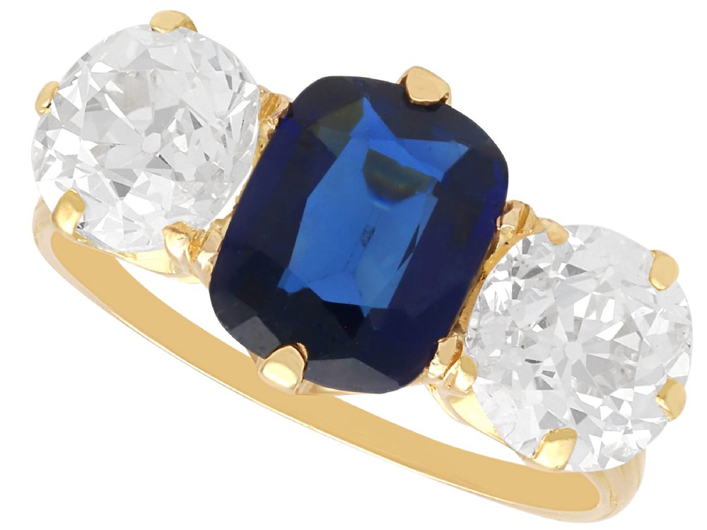An 18ct yellow gold Victorian trilogy ring set with a central cushion cut blue sapphire flanked by two round old cut diamonds.