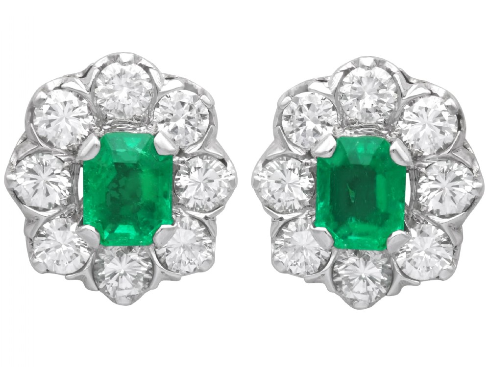 A pair of 18ct white gold cluster earrings featuring central emerald-cut green emeralds surrounded by a halo of round brilliant diamonds.