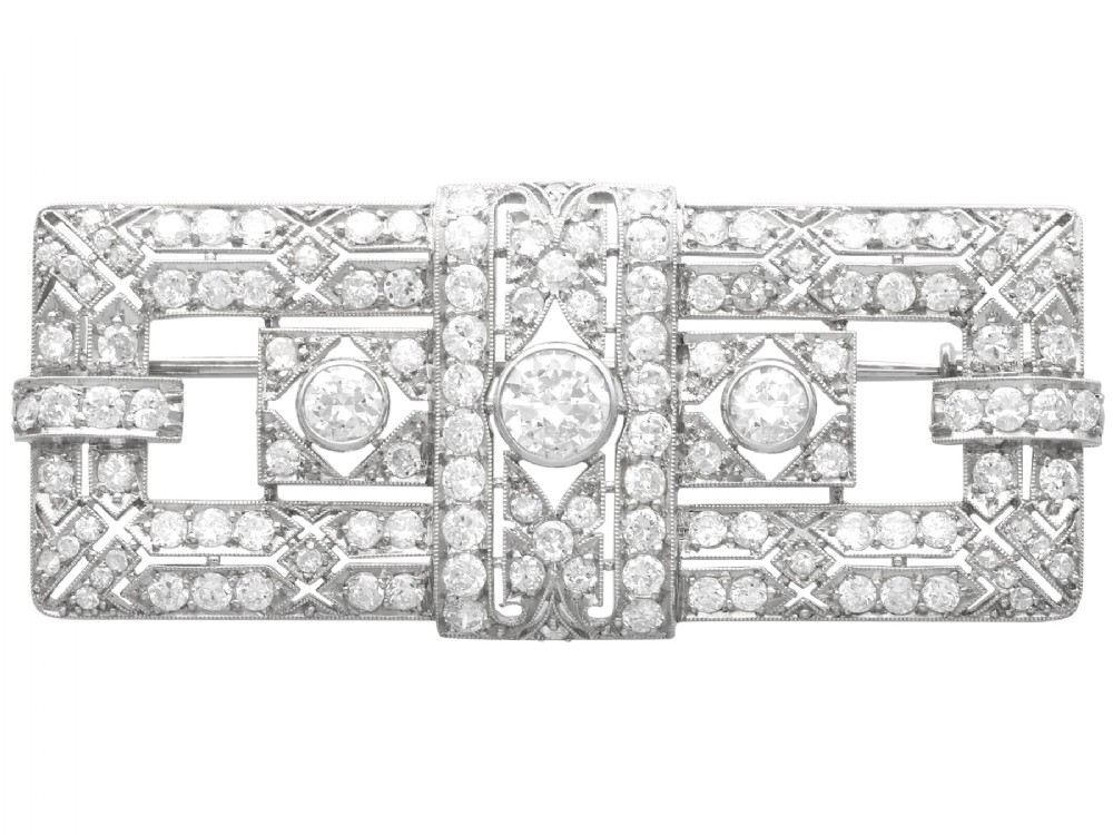 A rectangular Art Deco platinum brooch featuring intricate geometric openwork millegrain setting filled with round diamonds surrounding a central bezel-set diamond.