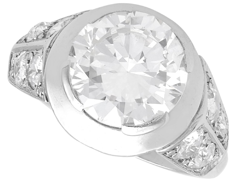 An Art Deco platinum ring featuring a central round diamond set in a smooth bezel with accent diamonds on the shoulders.