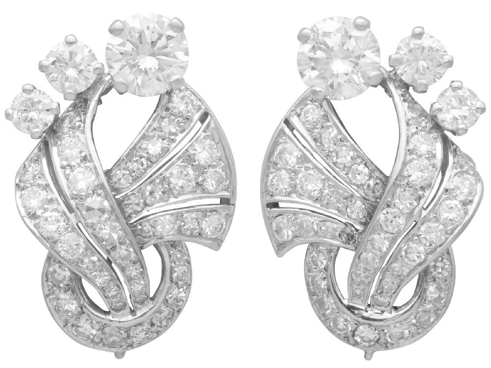 A pair of platinum earrings crafted in a sweeping fan and scroll design, fully set with brilliant-cut diamonds.