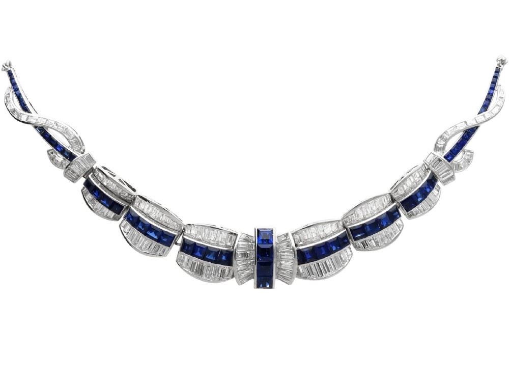 An Art Deco platinum collar necklace set with central square-cut blue sapphires bordered by baguette and round diamonds.