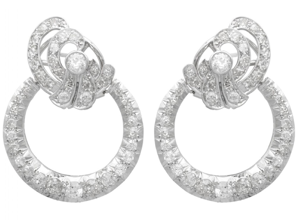 Pair of platinum clip-on earrings featuring circular diamond-set lower hoops suspended from geometric diamond scroll tops.