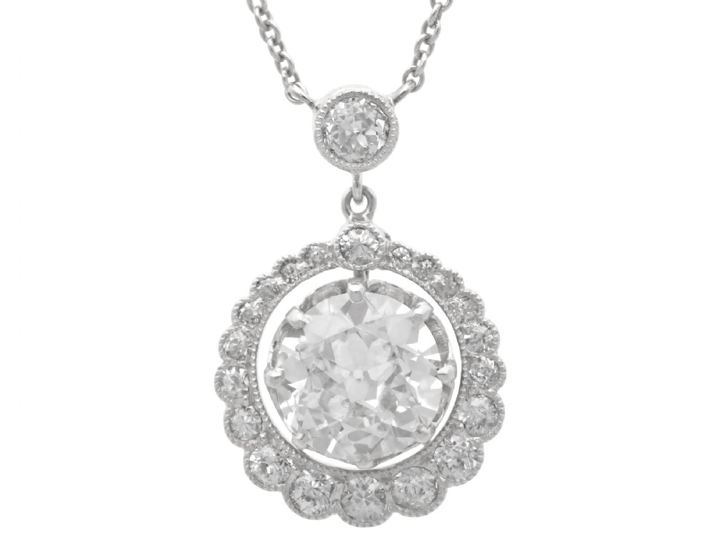 An antique platinum halo pendant featuring a central round diamond surrounded by a scalloped border of smaller diamonds on a fine chain.