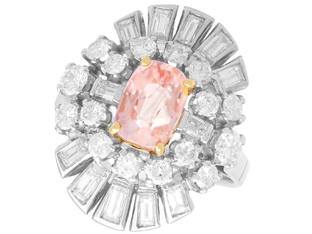 A platinum cluster ring featuring a cushion-cut pink sapphire set in yellow gold claws surrounded by diamond halos.