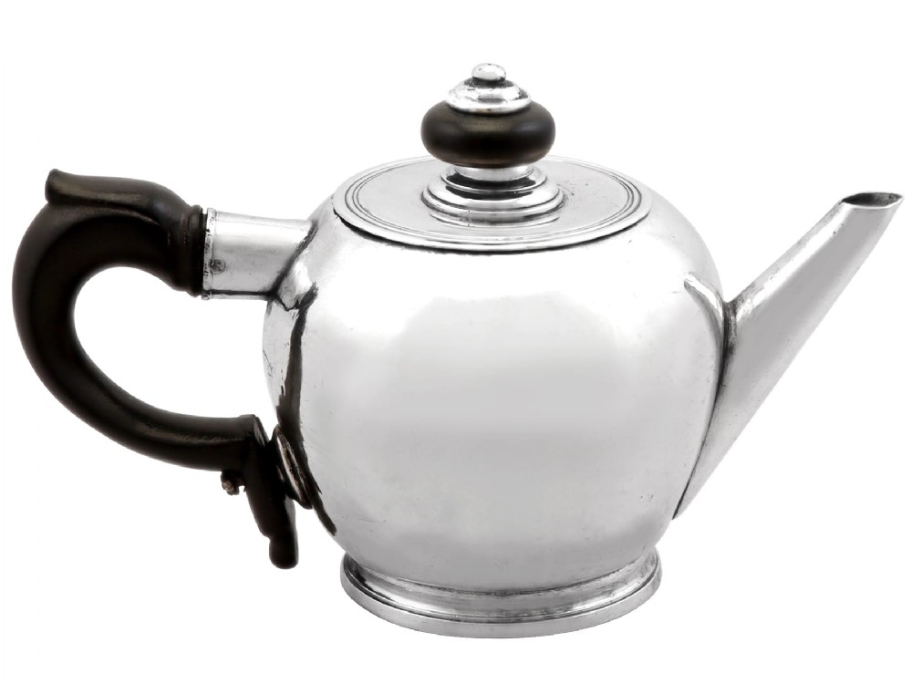 A George II period silver miniature herb teapot with a tapered spout, moulded foot rim, and carved dark wooden handle and finial.