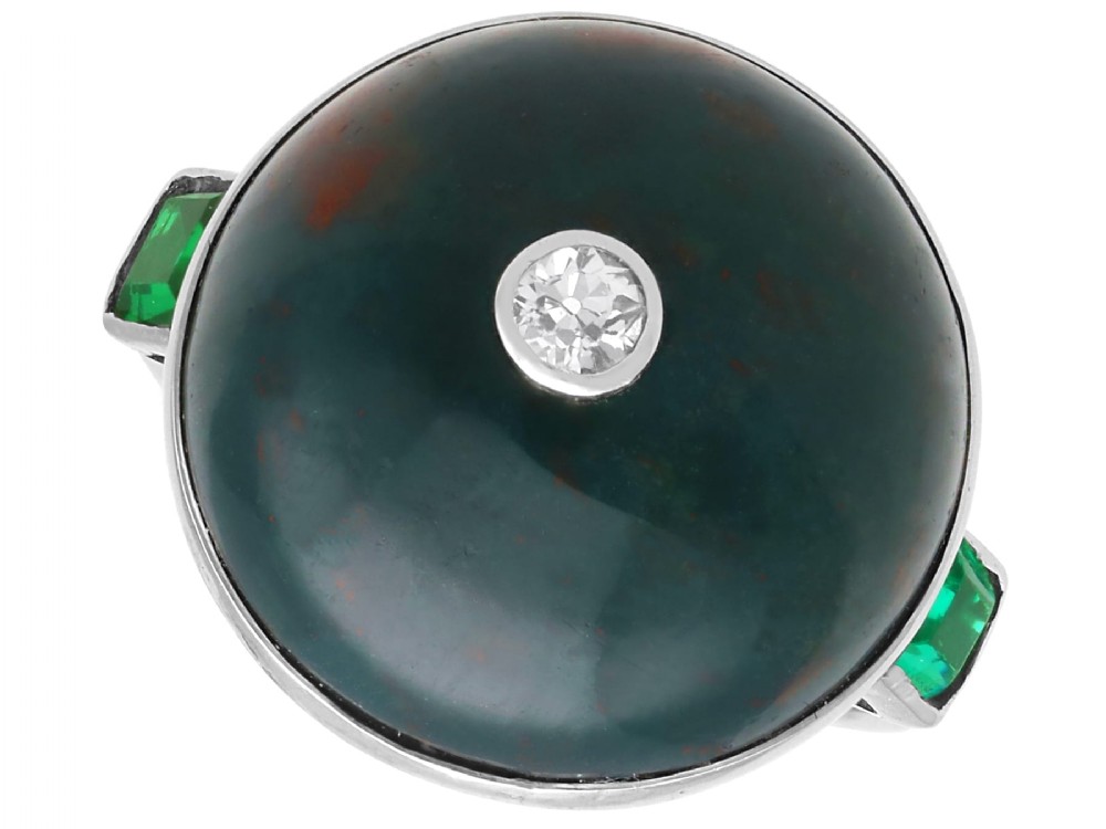 An antique circular bloodstone cabochon ring featuring a central inset diamond, mounted in 14ct white gold with green gem-set shoulders.