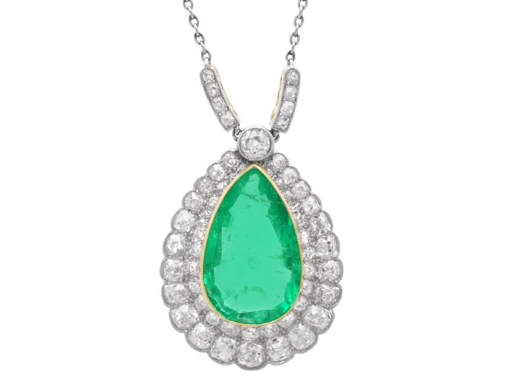 A pear-shaped green emerald surrounded by a halo of old-cut diamonds suspended from a diamond-set bale and fine chain.