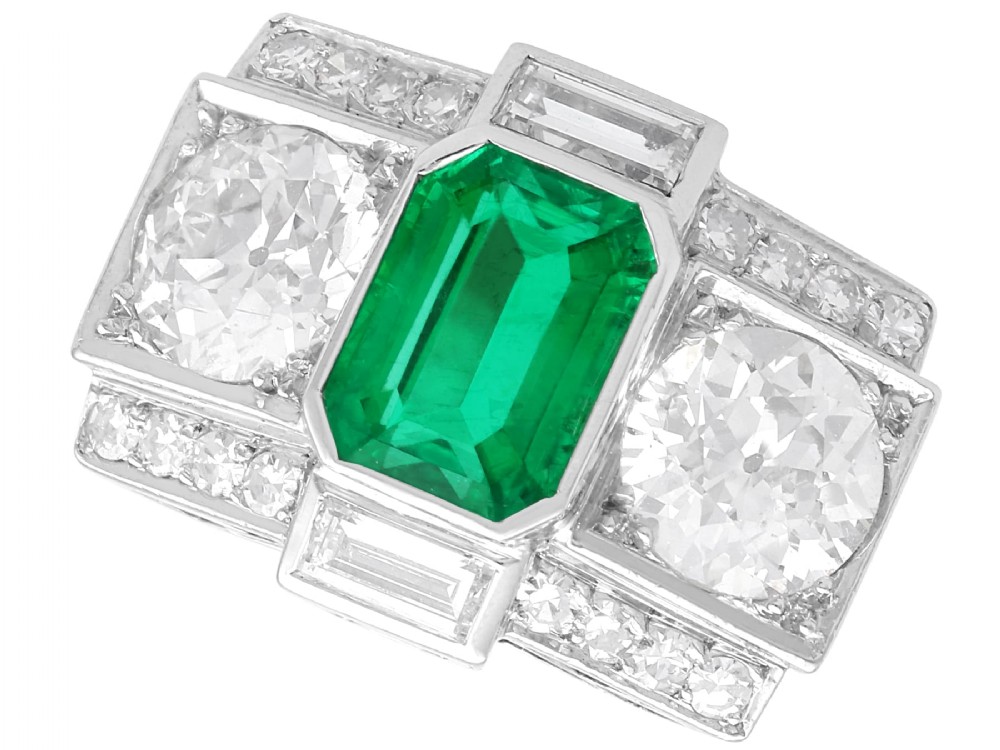 An Art Deco platinum cocktail ring set with a central rectangular emerald flanked by round diamonds and baguette diamonds.