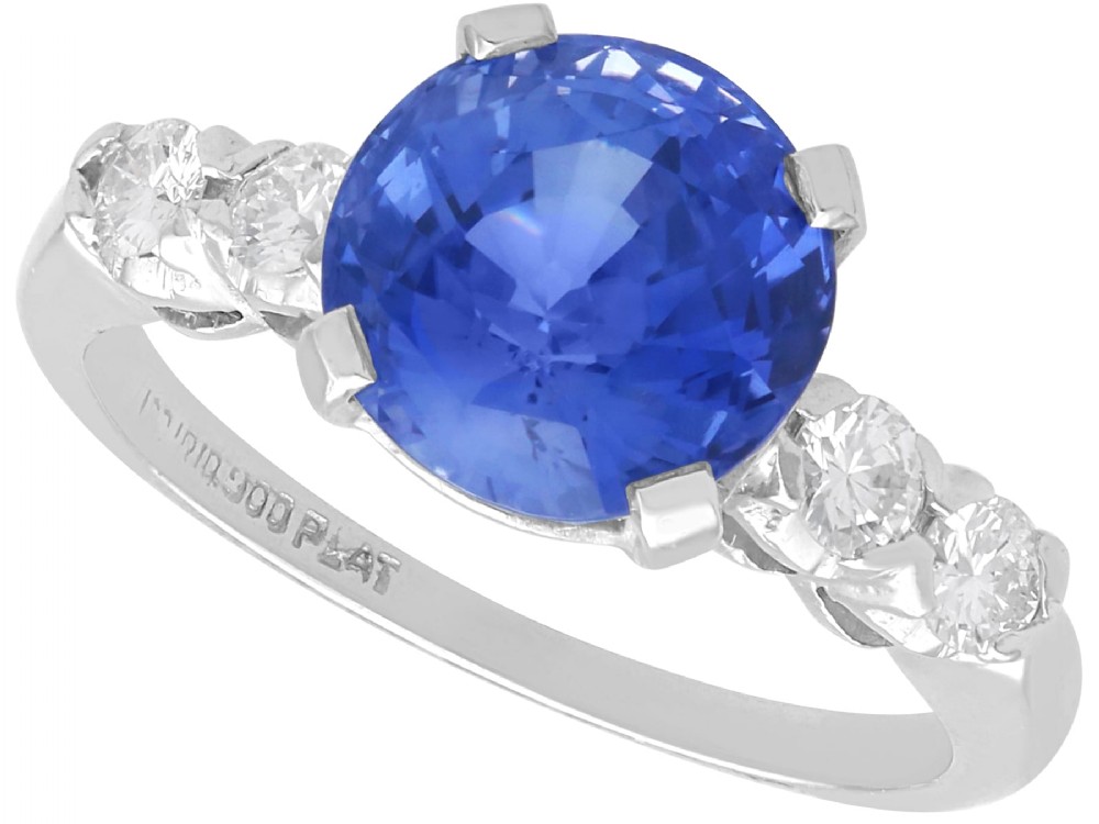 A round blue sapphire set in a platinum band flanked by round diamonds on each side.