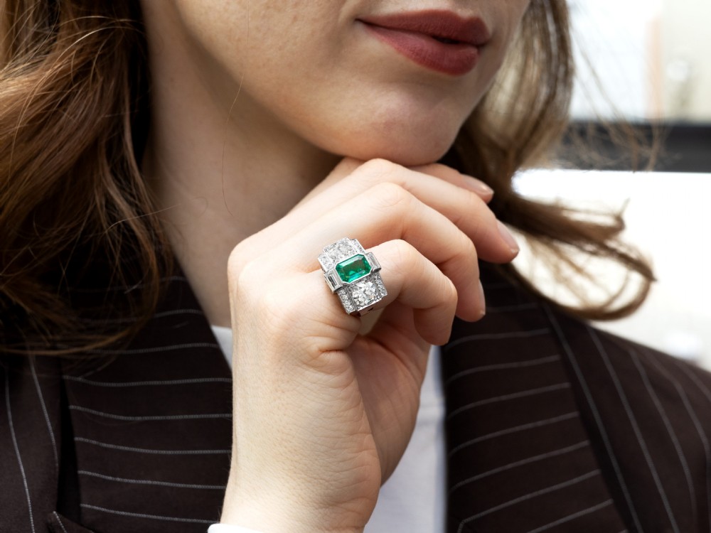 An Art Deco platinum cocktail ring set with a central rectangular emerald flanked by round diamonds and baguette diamonds. View VII