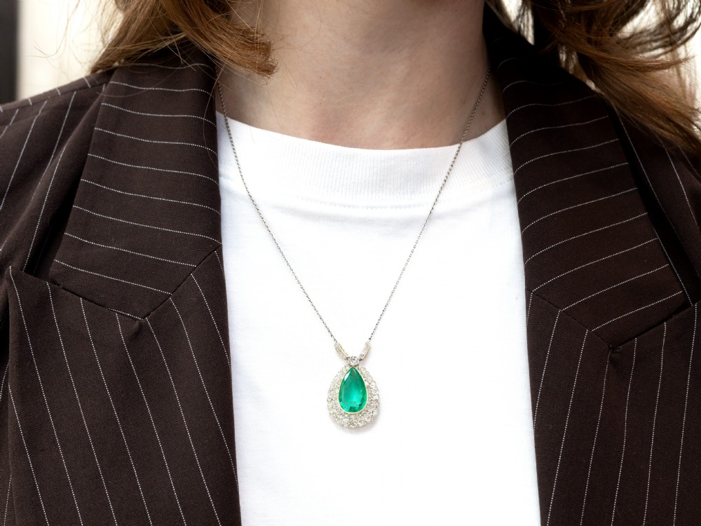 A pear-shaped green emerald surrounded by a halo of old-cut diamonds suspended from a diamond-set bale and fine chain. View VI