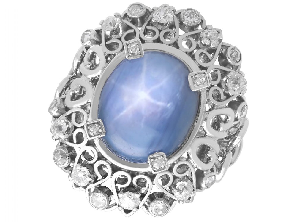 An oval cabochon blue star sapphire set in platinum surrounded by an intricate openwork diamond halo.