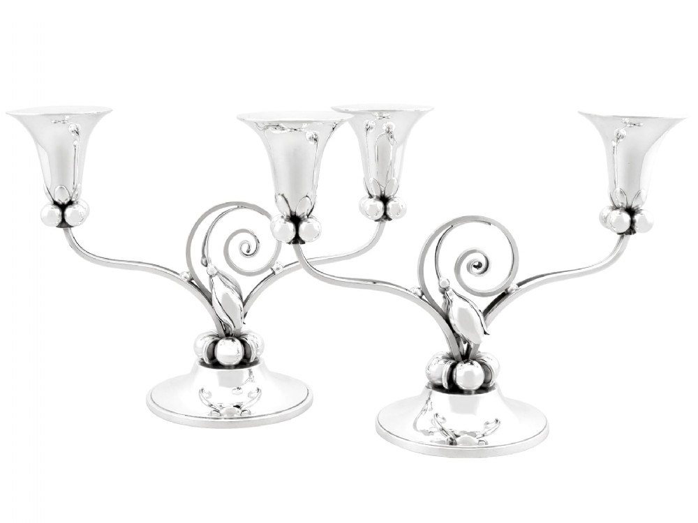 A pair of sterling silver two-light Arts and Crafts style candelabra featuring scrolled arms, beaded motifs, and flared sconces on circular bases.
