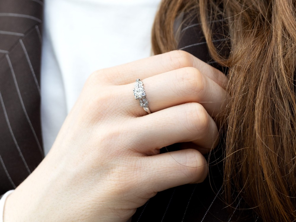 A platinum Art Deco solitaire ring featuring a central round diamond with geometric diamond-set shoulders. View IV