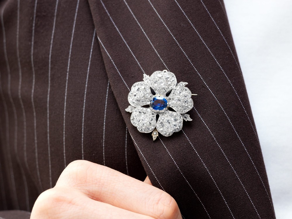 An antique Victorian silver pendant brooch featuring an oval blue sapphire centre surrounded by old-cut diamonds in a floral motif. View VII