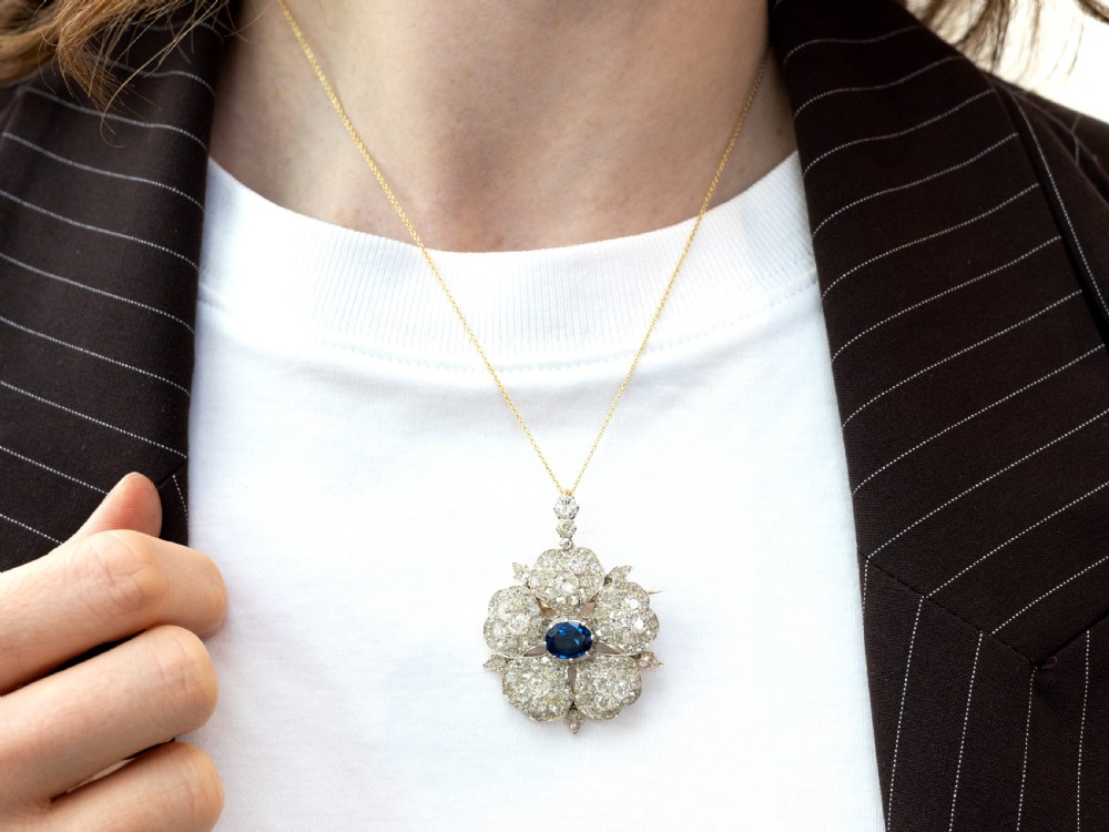 An antique Victorian silver pendant brooch featuring an oval blue sapphire centre surrounded by old-cut diamonds in a floral motif. View VIII
