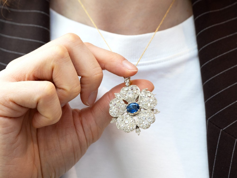 An antique Victorian silver pendant brooch featuring an oval blue sapphire centre surrounded by old-cut diamonds in a floral motif. View IX