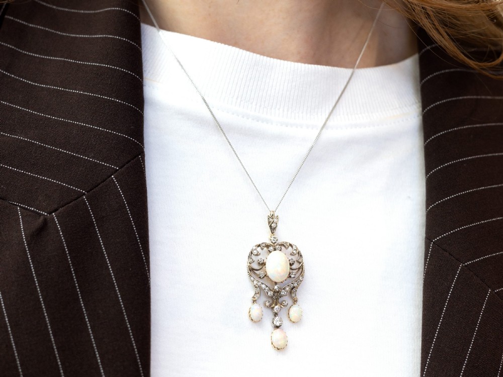 A late Victorian openwork silver and gold pendant featuring a central oval cabochon opal surrounded by diamonds and three suspended opal drops. View V