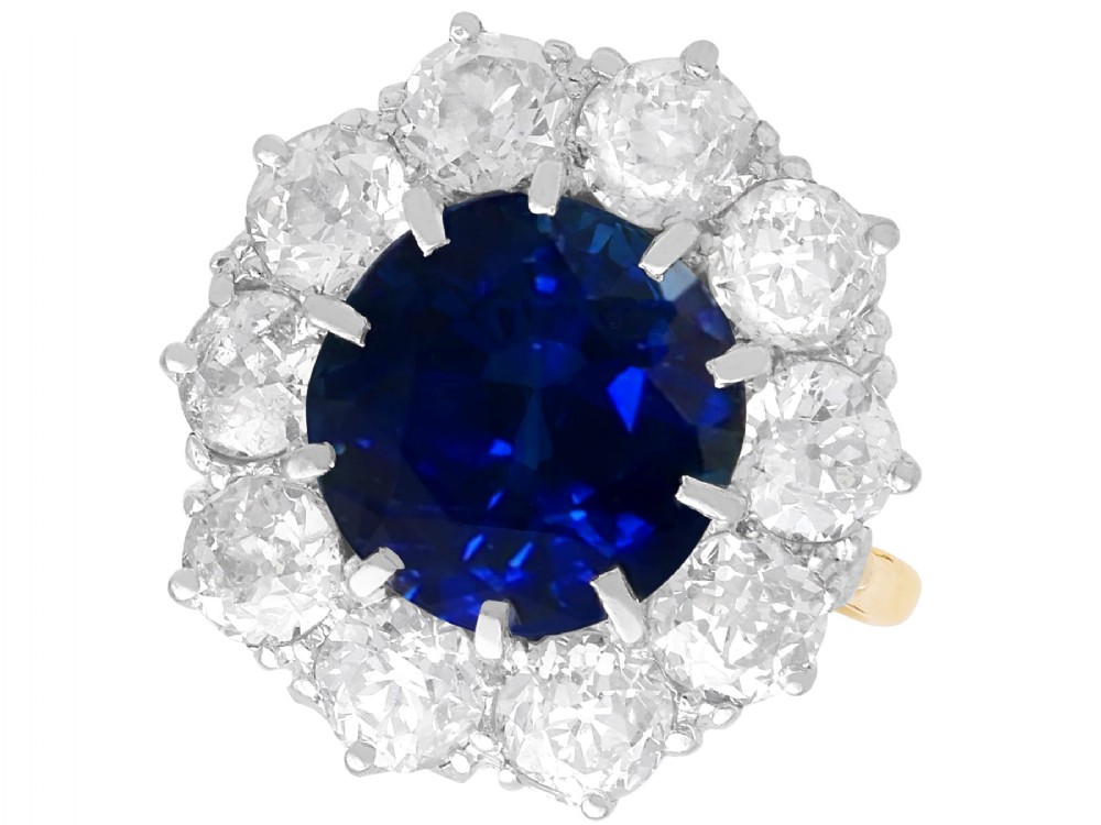 A round deep blue sapphire framed by a halo of ten round brilliant diamonds on an 18ct yellow gold band.
