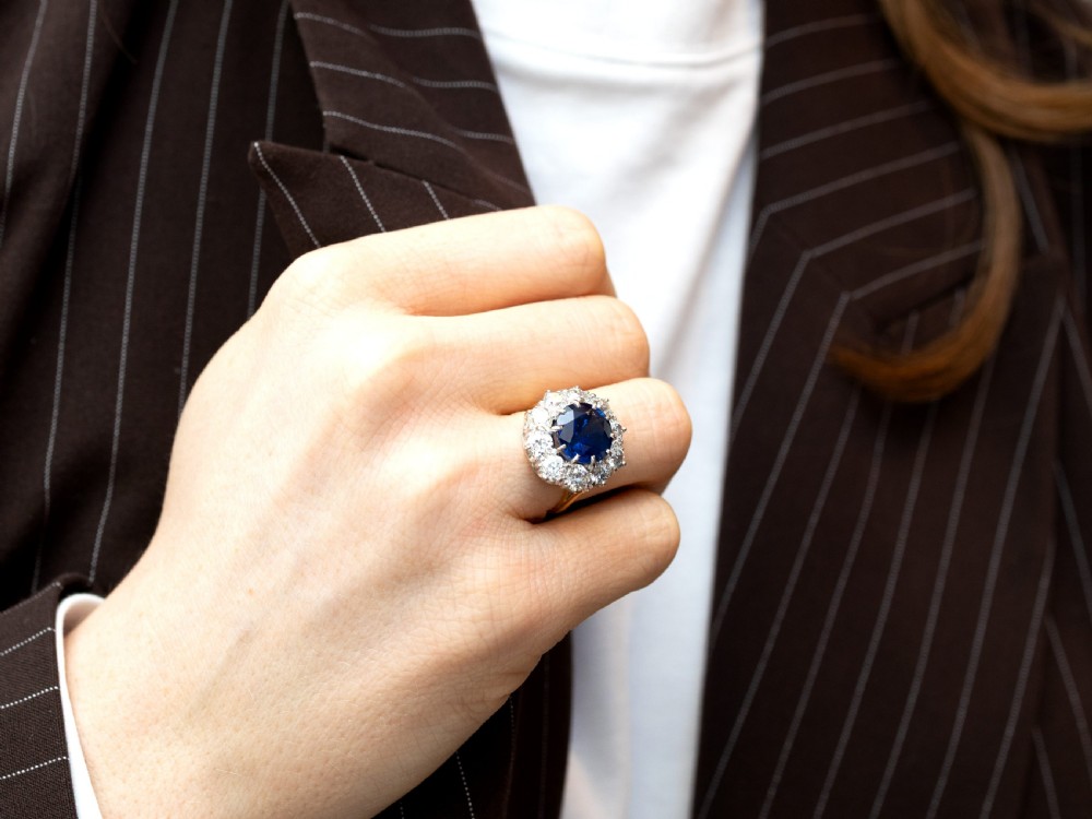 A round deep blue sapphire framed by a halo of ten round brilliant diamonds on an 18ct yellow gold band. View IV