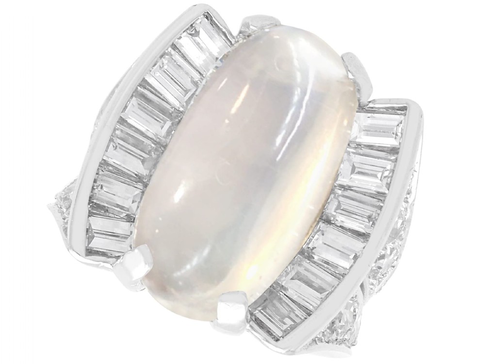 An Art Deco platinum dress ring featuring a central oval cabochon moonstone flanked by stepped baguette-cut diamonds.