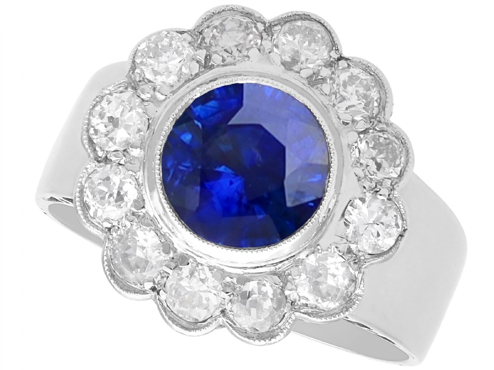 A vintage 18ct white gold cluster ring set with a central round blue sapphire surrounded by a halo of brilliant diamonds with a scalloped edge.