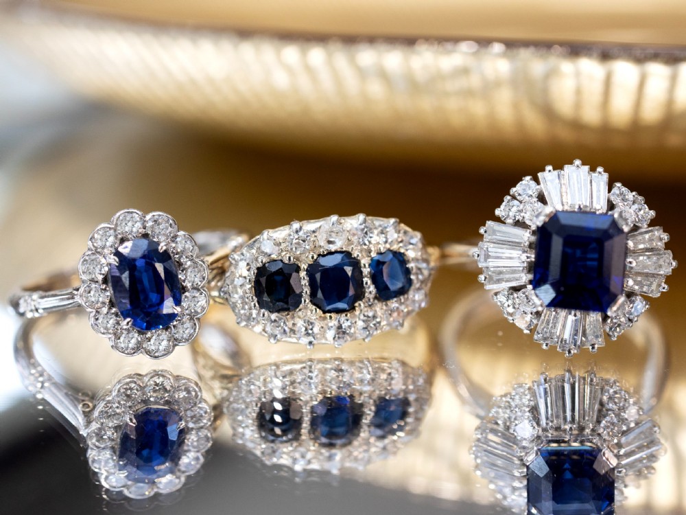 An Art Deco platinum ring featuring a central oval blue sapphire surrounded by a scalloped halo of round diamonds. View IV