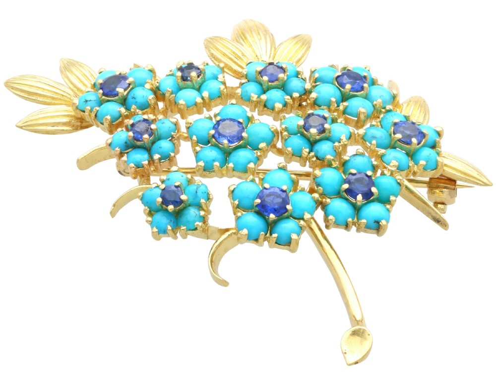 An 18ct yellow gold floral spray brooch featuring cluster settings of round blue sapphires surrounded by cabochon turquoise stones. View IV