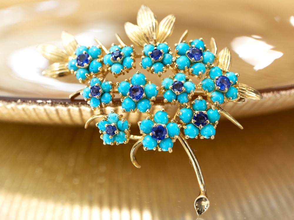 An 18ct yellow gold floral spray brooch featuring cluster settings of round blue sapphires surrounded by cabochon turquoise stones. View VI