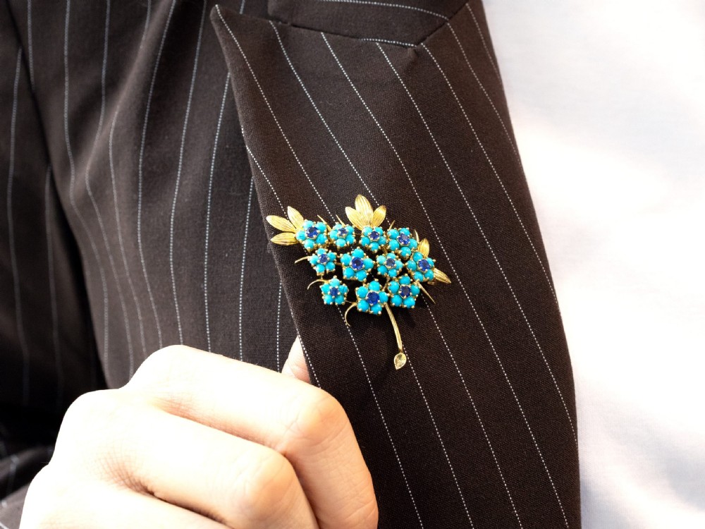An 18ct yellow gold floral spray brooch featuring cluster settings of round blue sapphires surrounded by cabochon turquoise stones. View VII