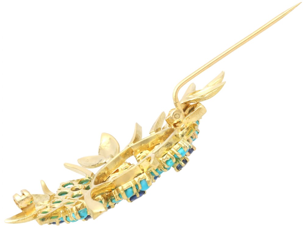 An 18ct yellow gold floral spray brooch featuring cluster settings of round blue sapphires surrounded by cabochon turquoise stones. View X
