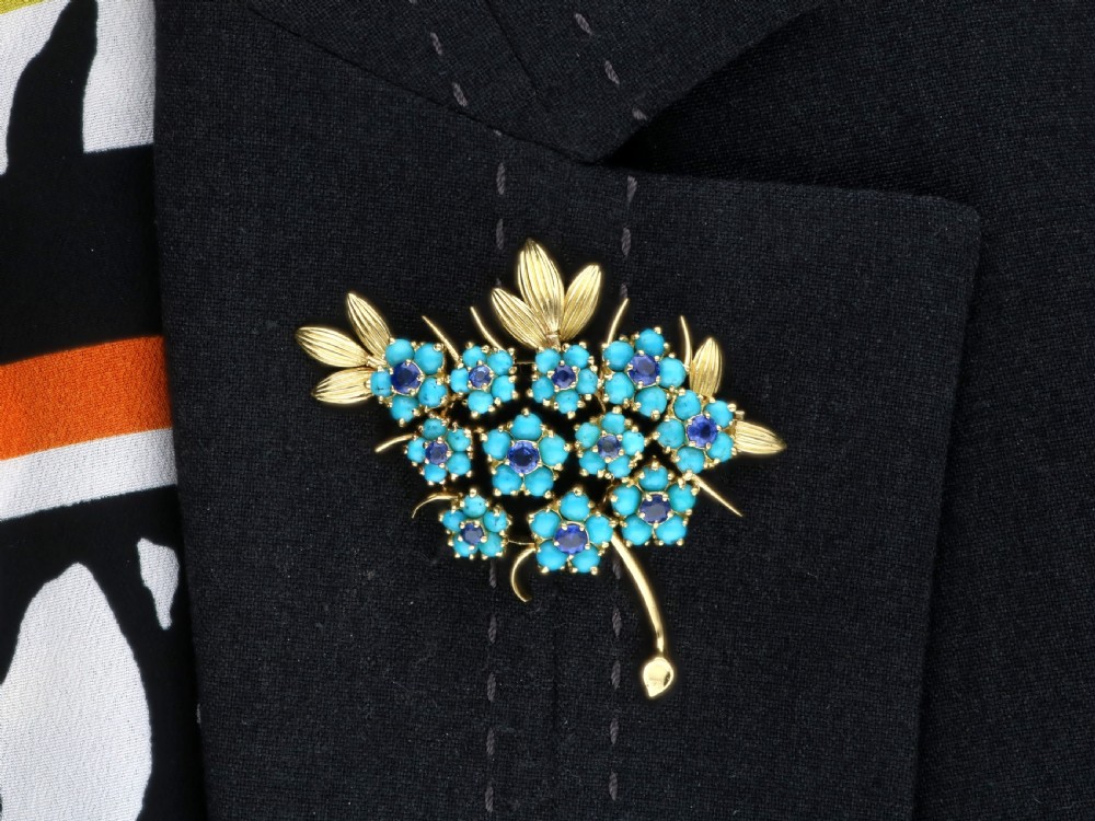 An 18ct yellow gold floral spray brooch featuring cluster settings of round blue sapphires surrounded by cabochon turquoise stones. View XIII