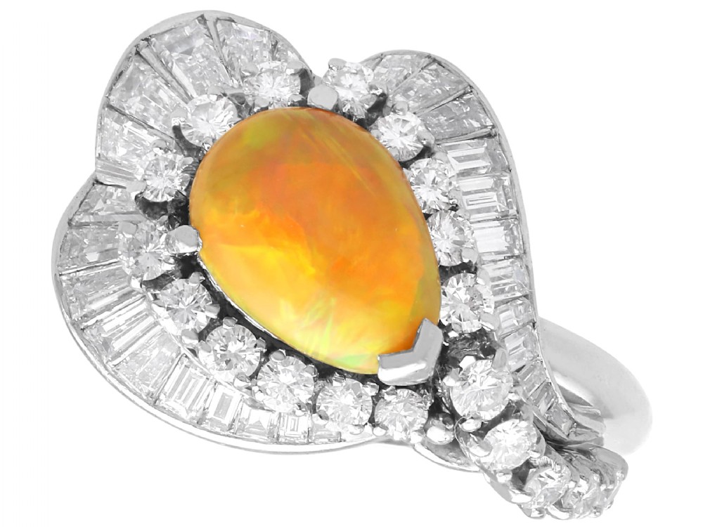 A platinum dress ring featuring a central pear-shaped orange opal surrounded by a halo of round and baguette-cut diamonds in an asymmetrical frame.