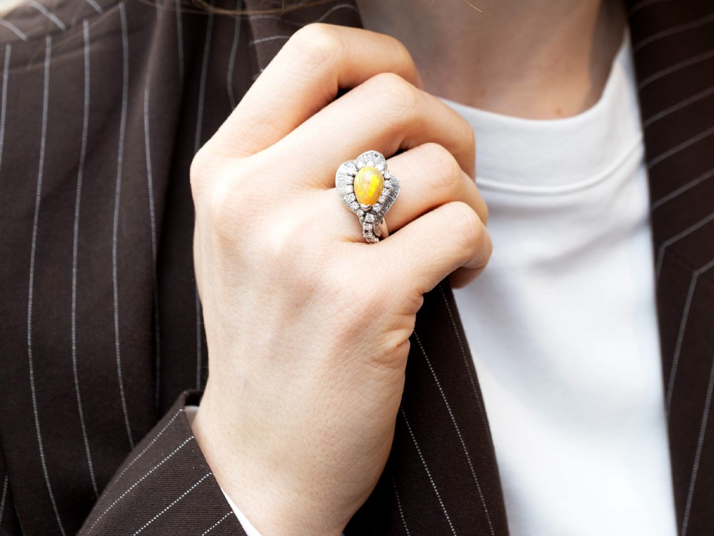 A platinum dress ring featuring a central pear-shaped orange opal surrounded by a halo of round and baguette-cut diamonds in an asymmetrical frame. View IV