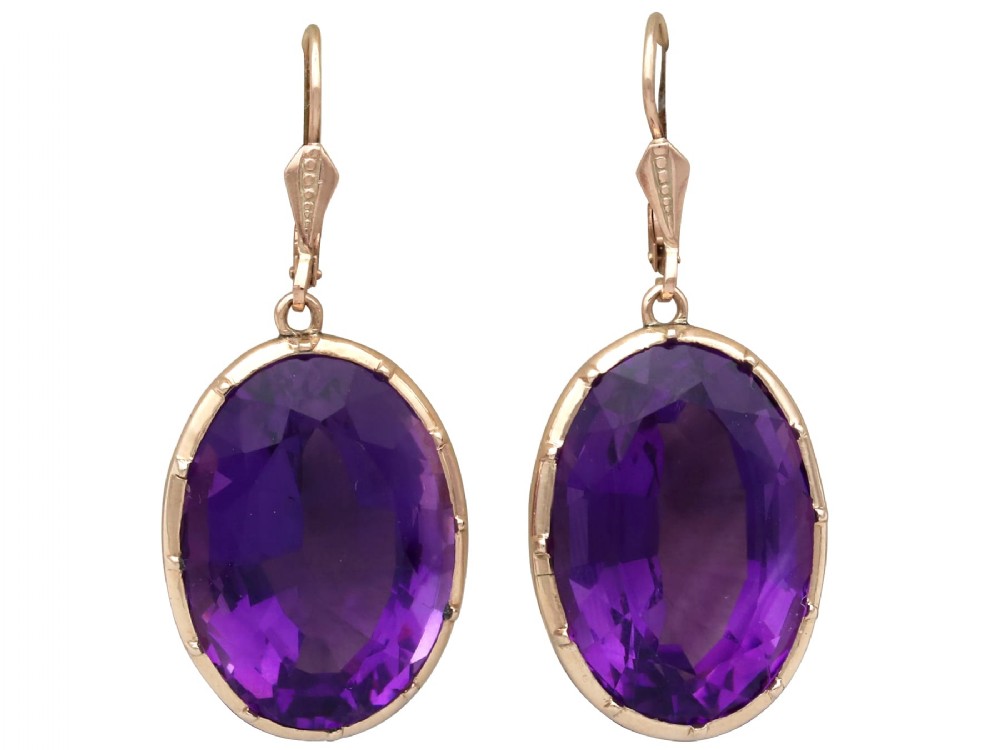 A pair of antique 9ct gold drop earrings featuring large oval faceted purple amethysts on leverback ear wires.