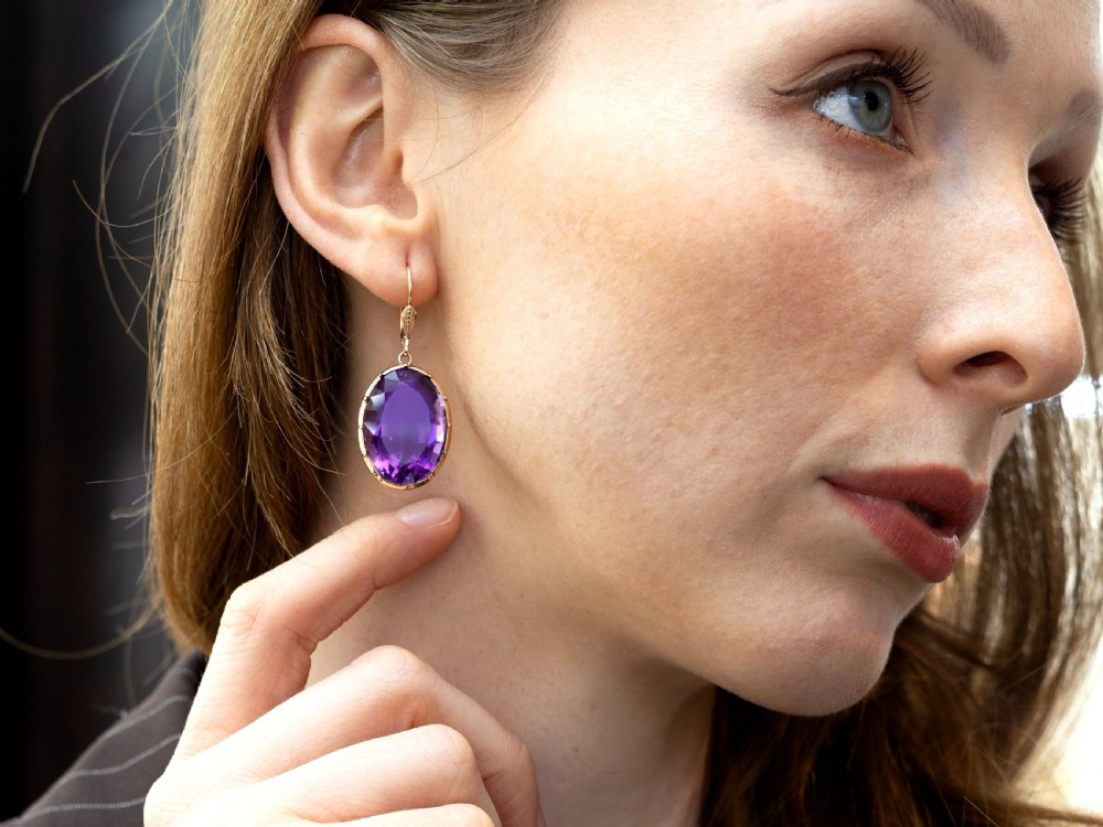 A pair of antique 9ct gold drop earrings featuring large oval faceted purple amethysts on leverback ear wires. View VI