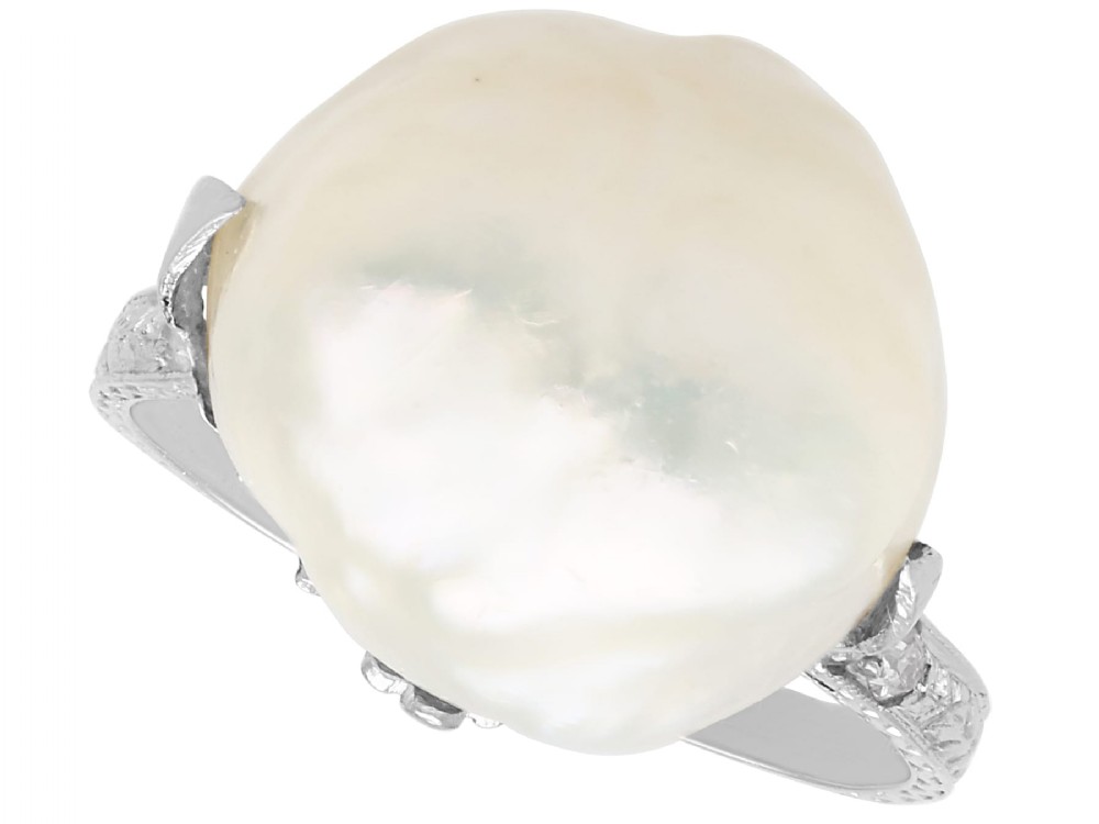 An antique platinum dress ring featuring a large, smooth natural blister pearl flanked by diamond-set shoulders.